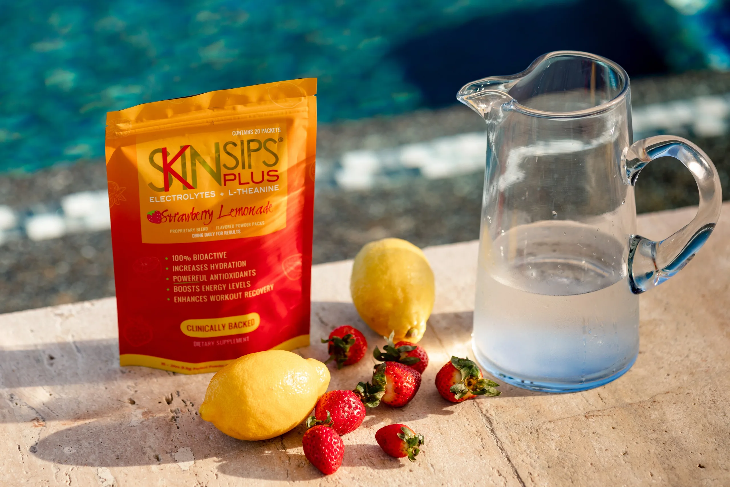 SkinSips Plus pouch beside a water pitcher, lemon, and strawberries by a pool. — skinsips plus pre-workout