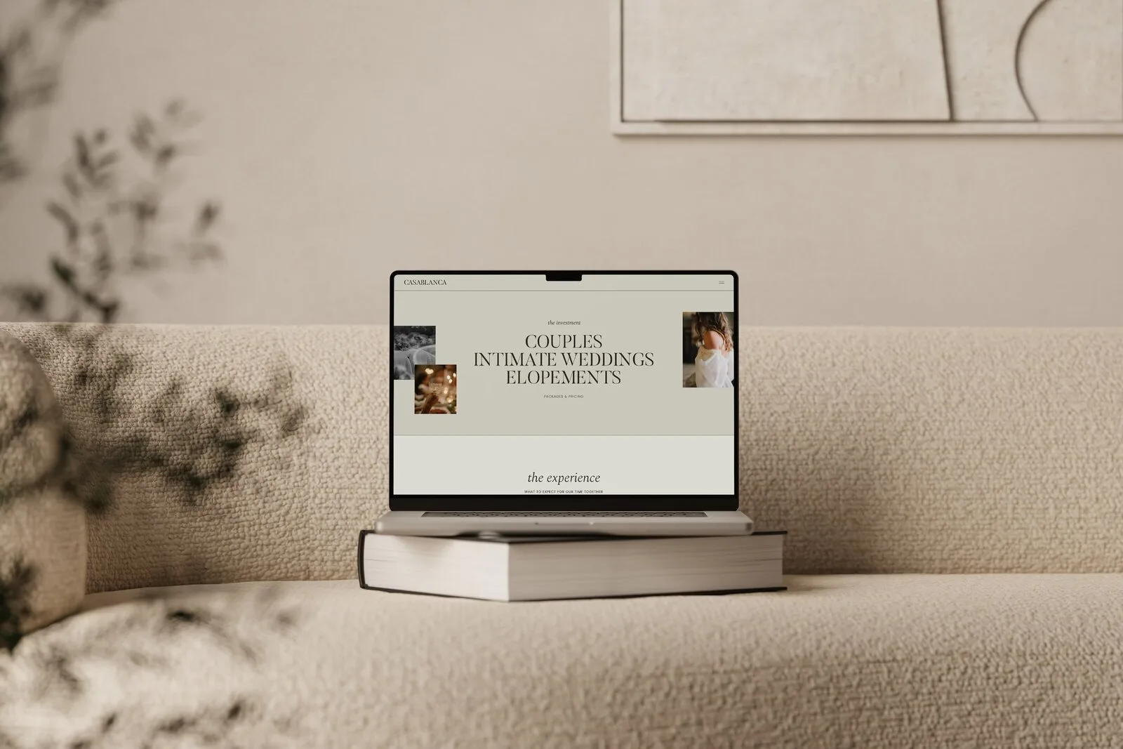 Laptop on stacked books showing a cream website mockup in a neutral room.