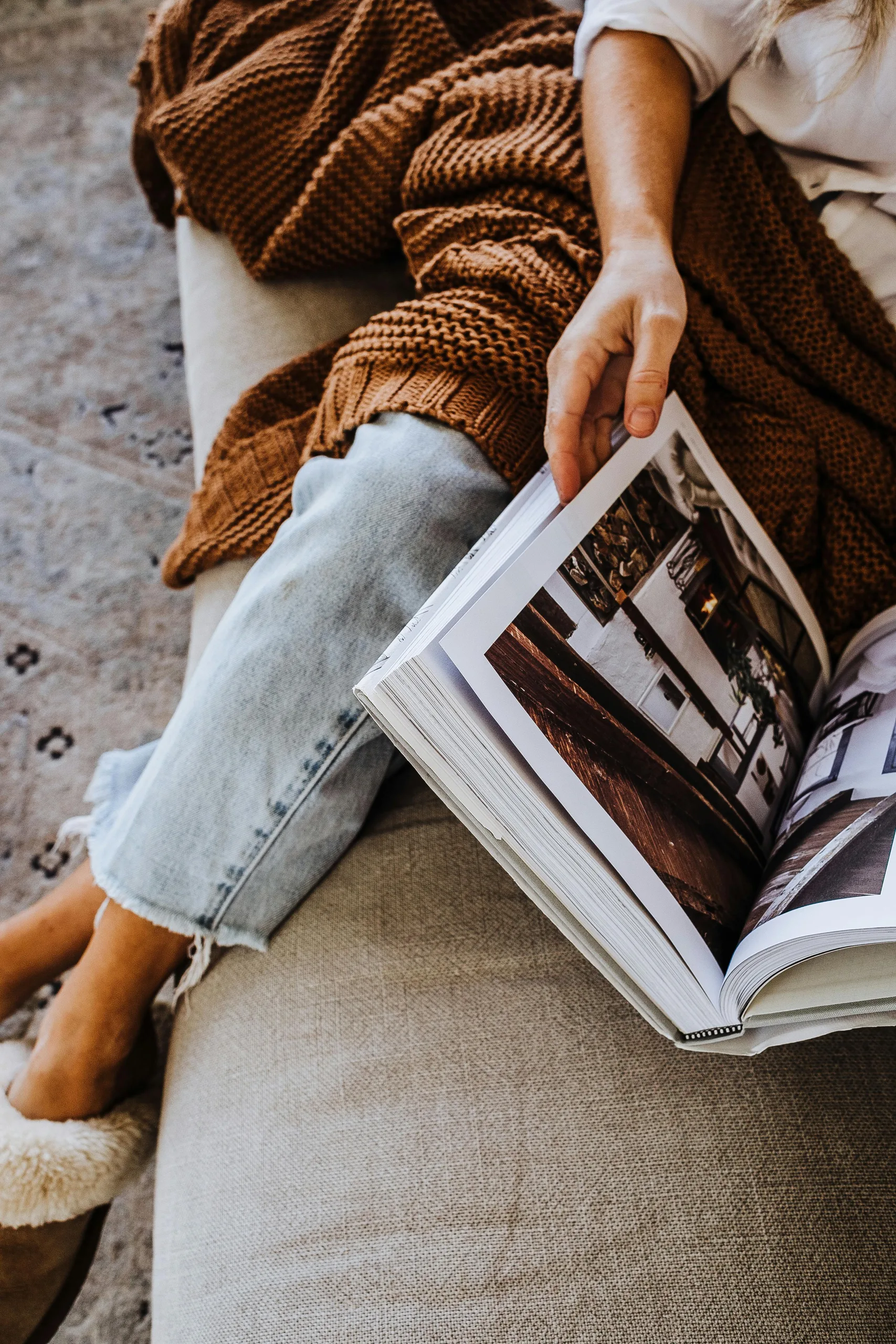Person on a beige couch reading an open magazine in soft warm light.