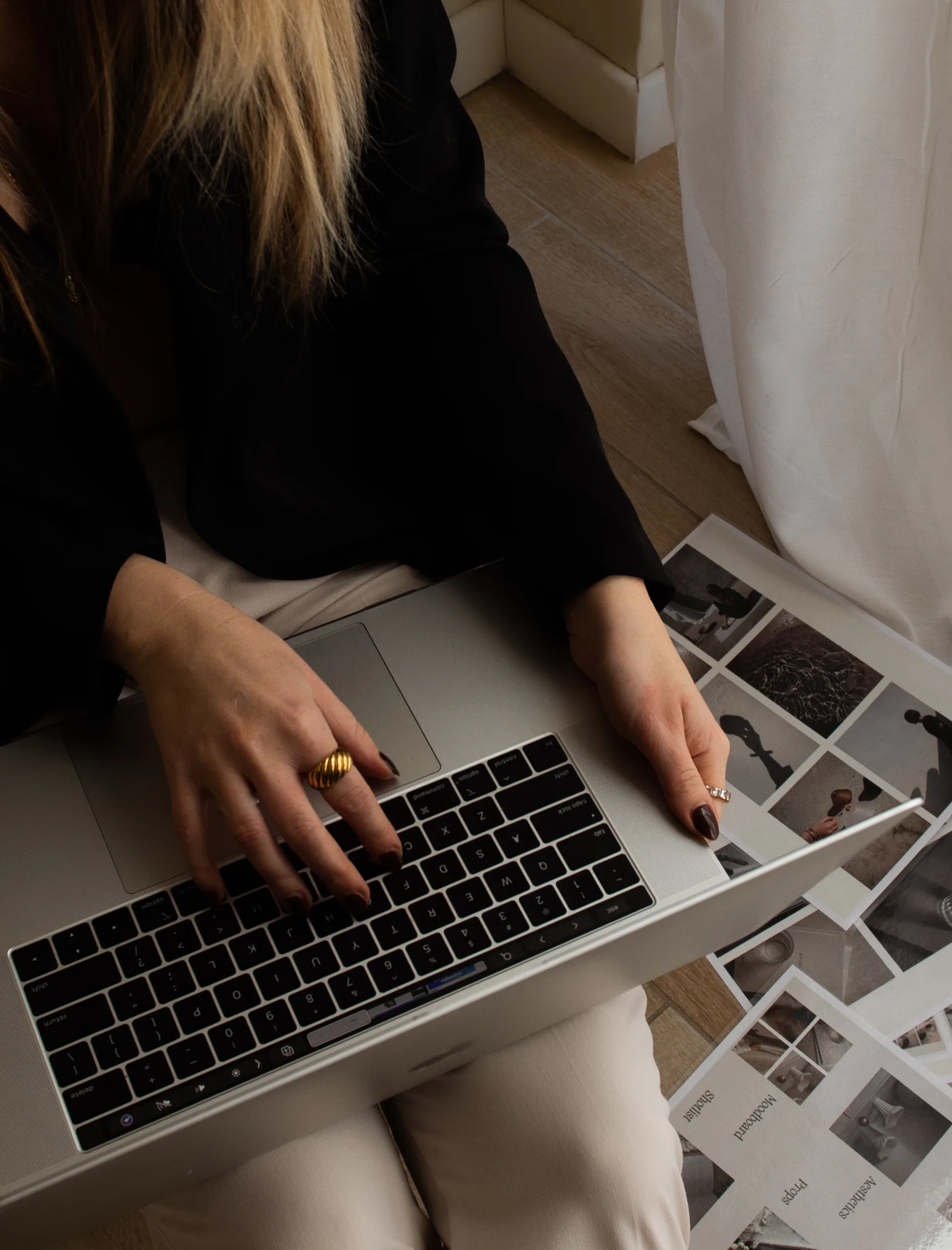 Person using a laptop beside printed page layouts on the floor.